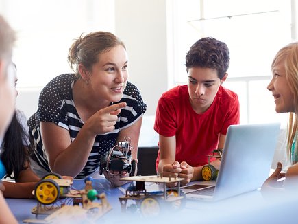 Woman with group of kids using laptop and engineering kits.jpg