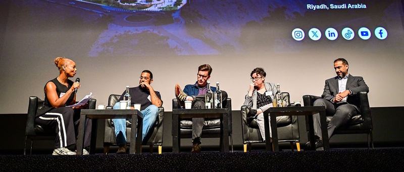 A panel of people on a stage - one has a microphone and is speaking as the others listen.