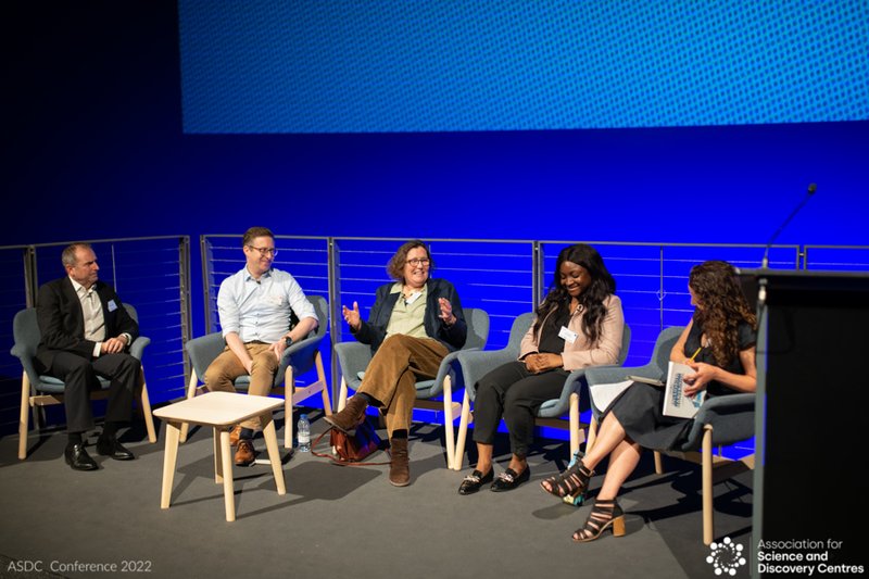 photo of a group of 5 people sitting on a stage talking to each other