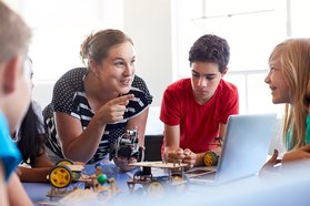 Woman with group of kids using laptop and engineering kits.jpg